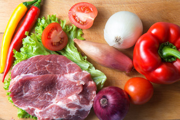 Pork-neck meat steaks on lettuce on background of radishes, tomato, red chili peppers, yellow chili peppers, green paprika, yellow paprika, red paprika, black pepper. Horizontal. Red onions, shallots