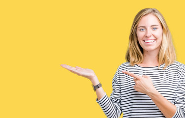 Beautiful young woman wearing stripes sweater over isolated background amazed and smiling to the camera while presenting with hand and pointing with finger.