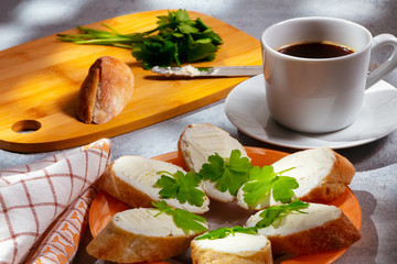 Freshly made sandwiches with cream cheese and parsley on a plate, chopping wooden board and a cup of coffee - morning and breakfast concept