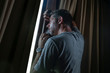 © TheVisualsYouNeed - dramatic light indoors portrait of young sad and depressed attractive man looking through home room window thoughtful and pensive in pain suffering depression problem
