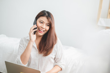 Beautiful Asian woman using laptop and smart phone in bed room for online shopping, Asian woman lifestyle concept