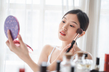 Wall Mural - Young beautiful Asian woman applying cosmetics make up on her face, health beauty skin care and make up concept