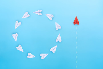Wall Mural - Group of white paper planes fly in a circle and one red paper plane pointing in different way on blue background. Business for new ideas creativity, innovative and solution concept.