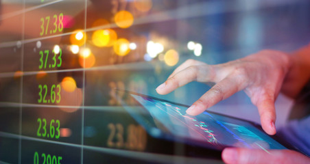 Businessman using tablet at night timeStock market. Businessman using a mobile device to check market data and currency exchange rates on colorful background.