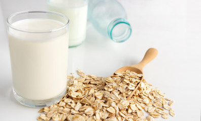 A glass of milk and oats in spoon on the white table. Its are a nutrient-rich food associated with protein and fiber.