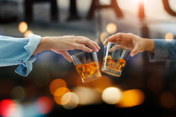 Close-up of two men clink glasses of whiskey drink alcoholic beverage together while at bar counter in the pub after work on colorful background