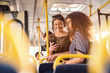 © dusanpetkovic1 - Two girls watching phone and smiling while standing on a bus.