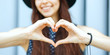 Closeup portrait of merry brunette model in hat making heart shape with her hands