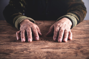 Old woman hands on wooden table.