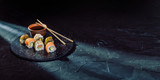 Fototapeta Tulipany - A different assortment of sushi rolls on a black coal board and a dark background. Traditional Japanese cuisine. Food with copy free space for text, logo