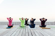 A group of people preparing for the morning yoga, girls do warm-ups on the open-air terrace near the sea. Students training in club, practicing yoga lesson with instructor outdoors