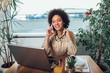 © Mediteraneo - Smiling young African female entrepreneur sitting at a desk in her home office working online with a laptop