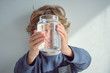 © ADDICTIVE STOCK - Cute little boy smiling and holding glass jar with clean water in front of face while standing near white wall