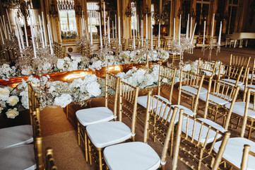 Wall Mural - Decorations for wedding dinner. Golden vases with candles stand on white tables ready for fesrive reception
