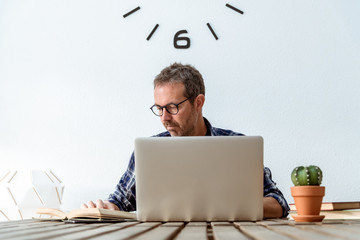 Business man computer student studying doing research using technology books professional sending mail middle-aged working from home while reading book writer engaged in writing novel Frontal portrait