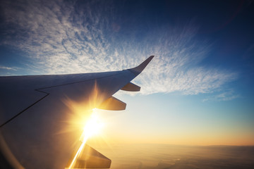 Poster - Sunset and wing of an airplane flying above the Earth. The view from an airplane window