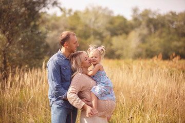 Portrait of pretty young pregnant woman with her young husband and cute little baby walking in park in sunny day. Family. Maternity. Happiness. Health.