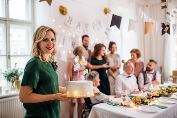 A young woman holding a birthday cake on an indoor party.