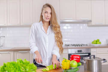 Happy young girl prepares healthy food in the kitchen slicing zucchini