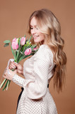 Fototapeta Tulipany - Happy beautiful elegant woman with pink bouquet of tulips over beige background.