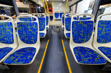 Bus inside, city transportation interior with blue seats in row, yellow handles for standing passengers and bright lights 