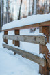 Photo of a wooden fence covered with snow, selective focus on the foreground, blurred background/ frosty winter day, cold snap, snowdrift, snowy winter, wooden bridge railing, winter park.