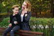 © Vagengeim - Young attractive mother and son in city park. Boy is sitting on bench and woman is hugging him from behind. Family time