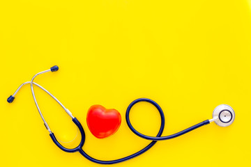 Wall Mural - Heart health, health care concept. Stethoscope near rubber heart on yellow background top view copy space