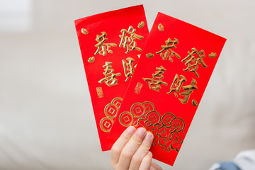 kid holding pair of red pockets written KUNG HEI FAT CHOY translation-wshing you prosperity