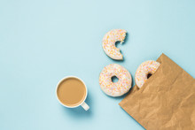 White Cup With Coffee Or Tea And Paper Bag With Fresh Delicious Sweet Donuts On A Blue Background. The Concept Of Fast Food, Bakery, Breakfast, Sweets. Minimalism. Flat Lay, Top View.