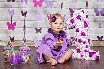 Little happy toddler girl celebrating first birthday. Cute baby girl sitting with big 1 and vase whith candy