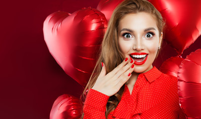 Happy young woman with heart balloons on red background. Surprised girl with red lips makeup and opened mouth. Surprise, sale, valentines people and Valentine's day concept