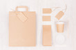 Coffee branding mockup - brown paper cup with blank bag, packet, label, cap, card, sugar on white wood board, top view.