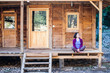 © zhukovvvlad - A woman is sitting on the porch of an old wooden house.