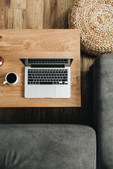 Wall Mural - Flat lay of home office desk workspace. Laptop, coffee cup on wooden table, sofa. Top view modern interior design concept.