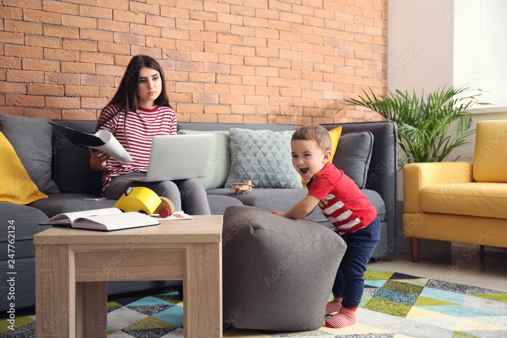 Cute little boy playing while his mother working at home
