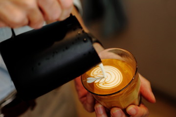 Wall Mural - Barista using pitcher for pouring frothed milk to cup of coffee latte with tulip pattern on top