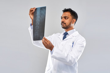 Wall Mural - medicine, healthcare and people concept - indian doctor looking at spine x-ray over grey background