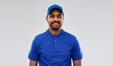Mail Service, Job And People Concept - Happy Indian Delivery Man In Blue Uniform Over Grey Background