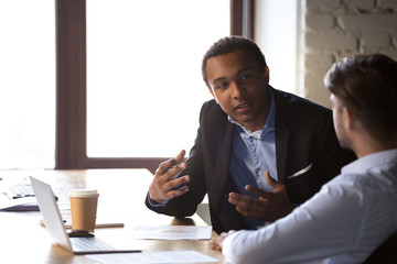 Diverse employees negotiate gesturing near laptop in office