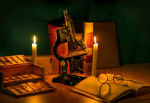 Historisches Mikroskop Stilleben Mit Buch, Brille Und Kerzenlicht. Geschichte Der Mikroskopie Wissenschaft