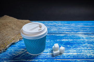 Blue disposable cup with fragrant coffee on a wooden background with refined sugar near