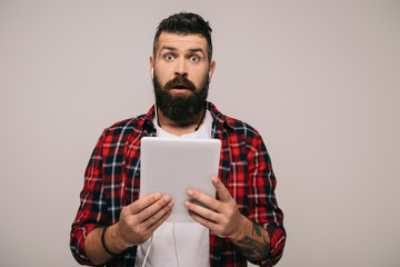 Wall Mural - shocked bearded man with earphones holding digital tablet, isolated on grey