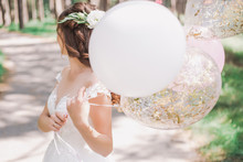 Beautiful Young Bride Holding Several Air Balloons In Hands While Standing Outside On Sunny Warm Day. Horizontal Color Photography.