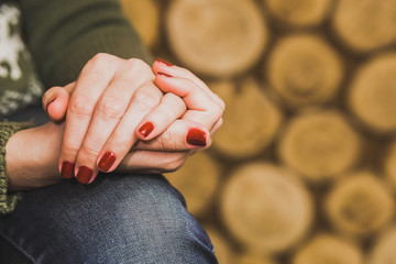 Woman sitting calmly in home interior. Closeup view of two female hands resting on her knee. Fingernails wit red glossy sparkling manicure, Horizontal color photography.