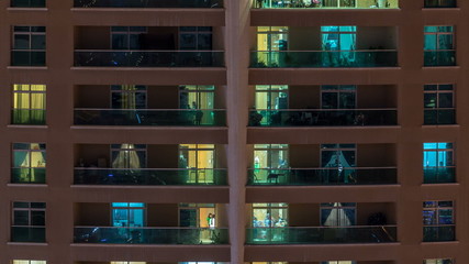 Glowing windows in multistory modern glass residential building light up at night timelapse.