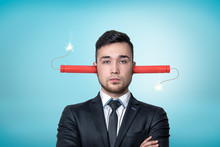 Crop View Of A Businessman, Arms Folded, Burning Dynamite Sticks Up His Ears, On A Light-blue Background.