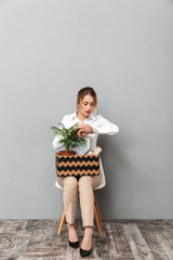 Canvas Print - Portrait of european woman holding box with office belongings while sitting in chair, isolated over gray background