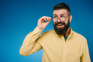 Wall Mural - smiling handsome man in eyeglasses isolated on blue