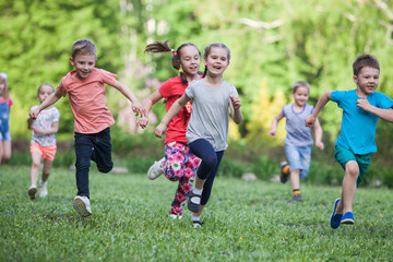 A group of happy children of boys and girls run in the Park on the grass on a Sunny summer day . The concept of ethnic friendship, peace, kindness, childhood.